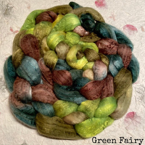 A braid of  soft hand dyed IxCHeL cashmerino silk top fibre Fiber in mixed pastel and earthy colours including green, blue, pink, brown, and beige, photographed on a light textured hand made paper surface with the text 'Green Fairy' in the lower right corner. 