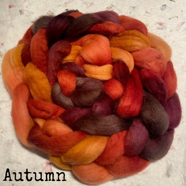 An IxCHeL hand dyed bundle of soft, fool earth top roving in an autumn colorway, featuring shades of orange, red, rust, mustard yellow, and deep plum, with the word 'Autumn' printed in black text in the bottom-left corner.