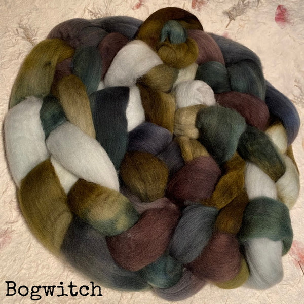 A braided hand dyed IxCHeL yarns and fibres  bundle of multi-coloured Polwarth wool roving top labeled 'Bogwitch' in black text at the bottom left, photographed on a light textured handmade paper background.