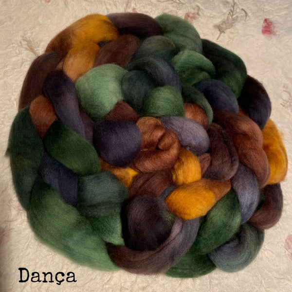 A braid of soft, hand dyed IxCHeL wool roving polwarth top in a colourway of forest green, dark purple, brown, and mustard yellow, labeled 'Danca' on a textured handmade paper background.