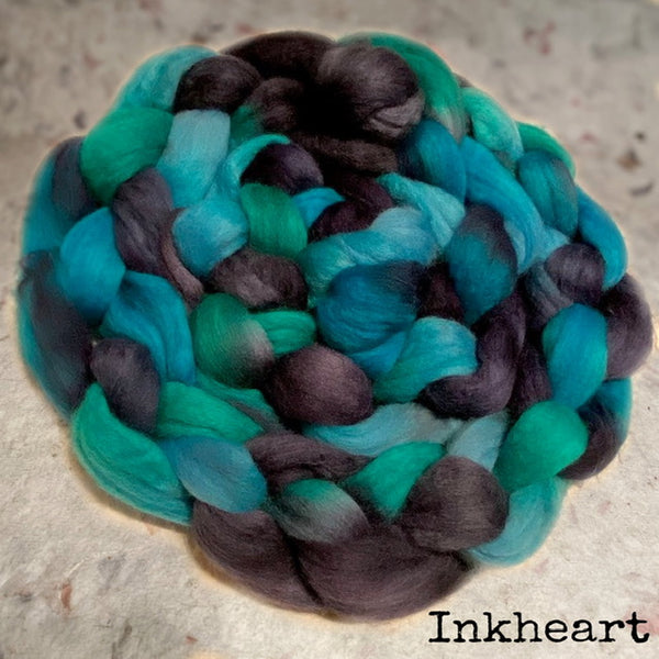 An IxCHeL  of soft, fuzzy Polwarth top in a variegated blend of teal, turquoise, mint green, and dark charcoal grey. The name 'Inkheart' is printed in black text in the bottom right corner.