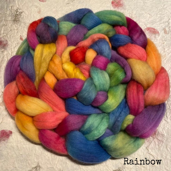 An IxCHeL hand dyed bundle of soft, Polwarth top roving in a rainbow colours including blue, green, yellow, orange, pink, and purple. Text 'Rainbow' in the bottom right corner.