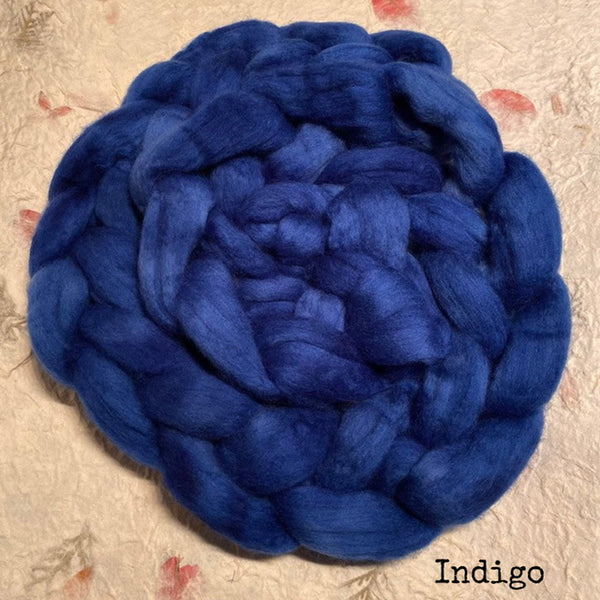 An IxCHeL hand dyed braid  of fluffy polwarth wool roving top in a deep indigo blue,  with the word 'Indigo' printed in the bottom right corner.